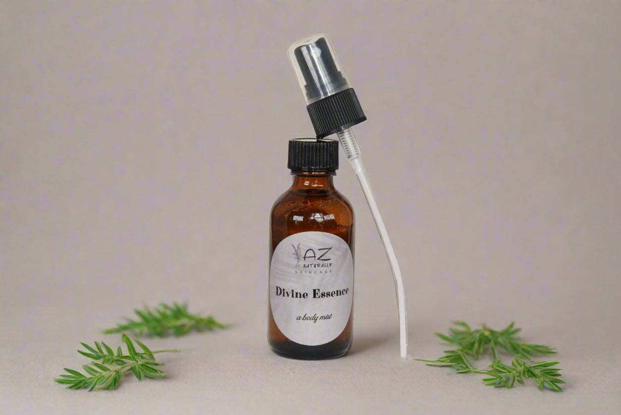 Amber dropper bottle of 'Divine Essence - A Room/Body Mist' with a spray top on a light gray background beside leaves 