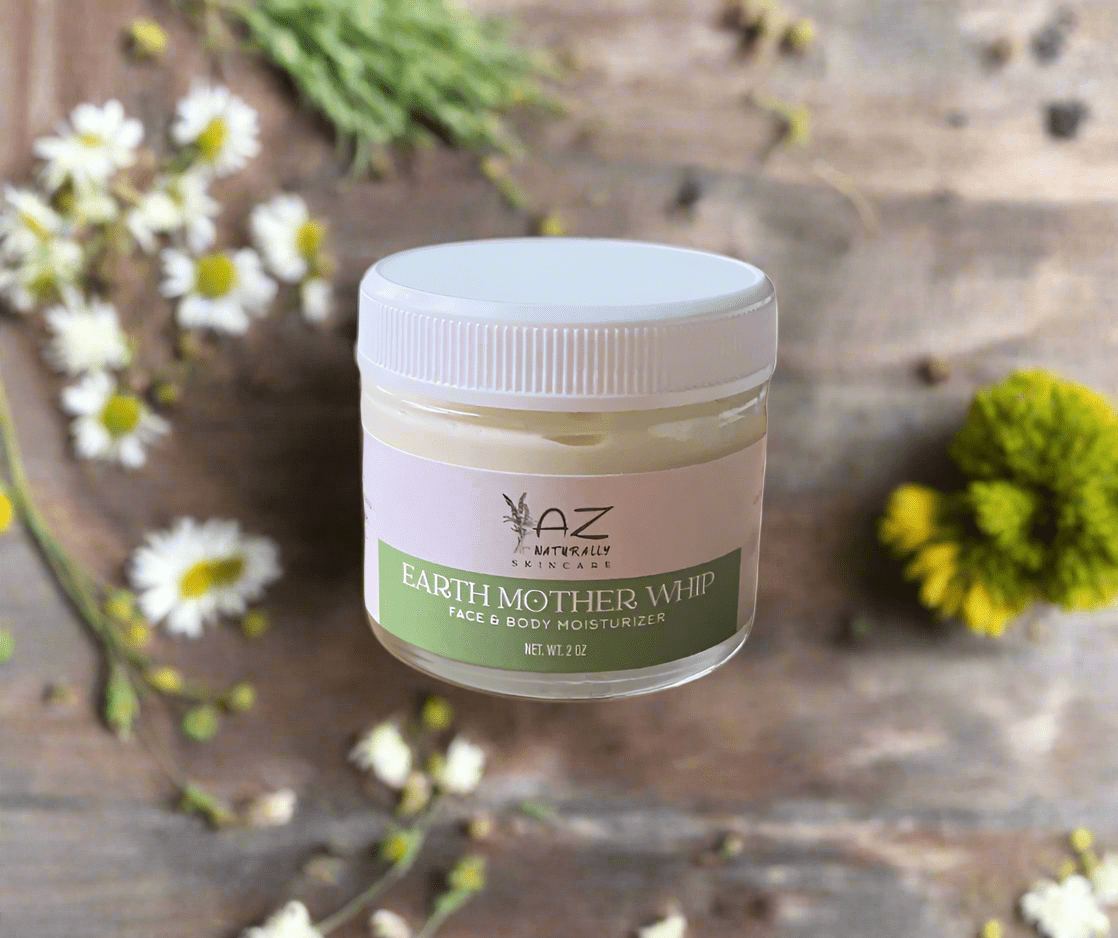 Jar of 'Earth Mother Whip' face and body moisturizer on with white and yellow flowers on a wooden surface