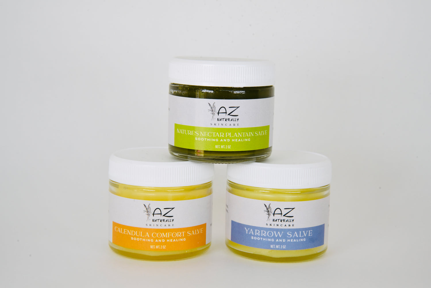Three jars of herbal salve labeled 'Plaintain Salve', 'Calendula Salve', and 'Yarrow Salve' on a light gray background