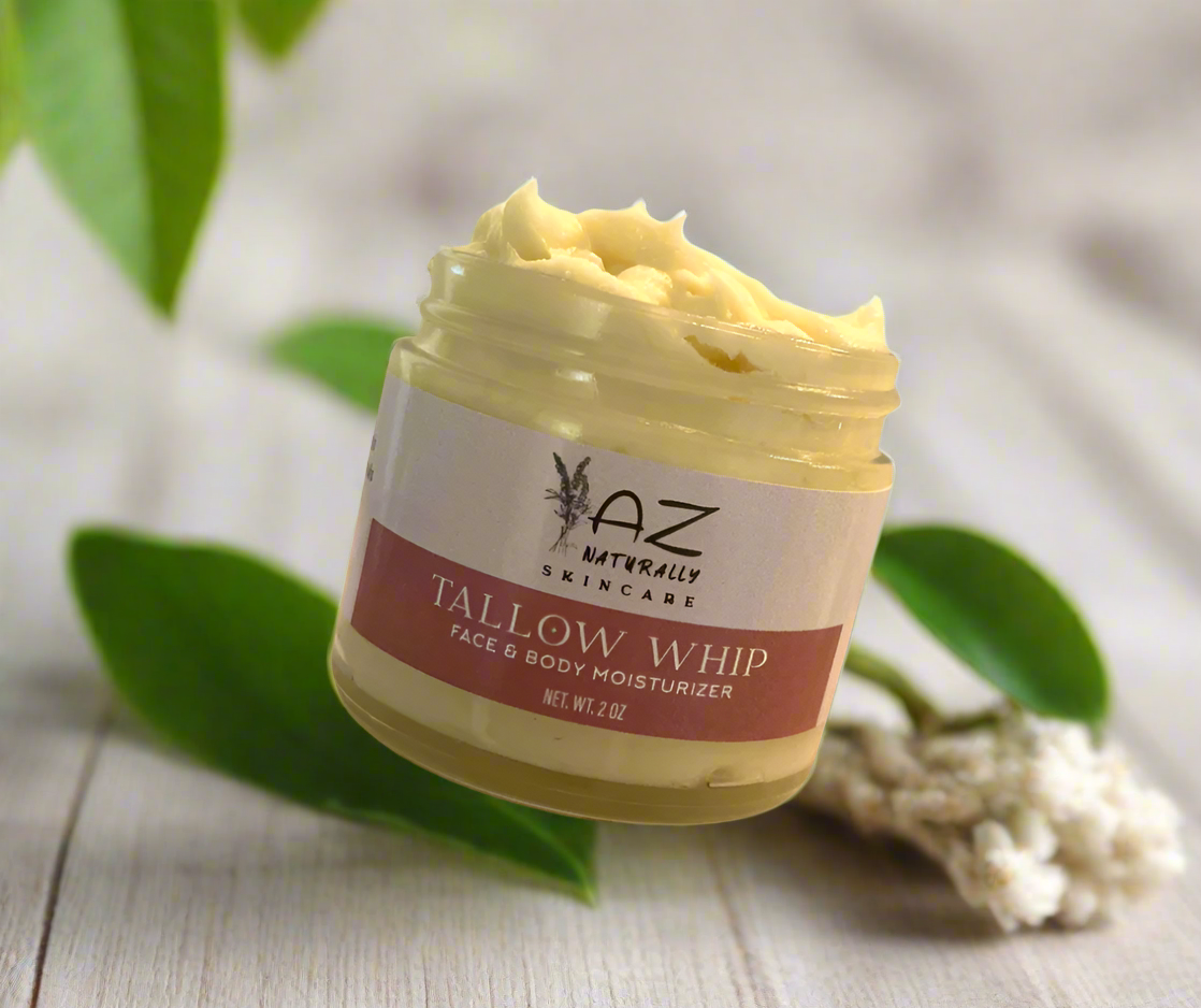 An open jar of 'Tallow Whip Face and Body Moisturizer' on a light gray background with leaves
