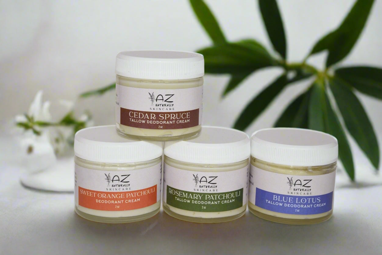 Four jars of 'Tallow Deodorant Cream' labeled 'Sweet Orange Patchouli', 'Cedar Spruce', 'Rosemary Patchouli', and 'Blue Lotus' on a light gray surface with a leaf in the background 