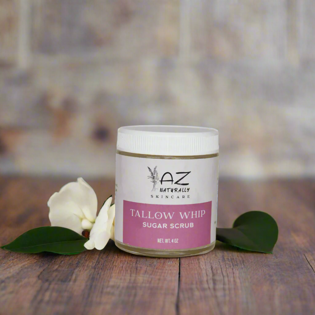 Jar of 'Tallow Whip Sugar Scrub' surrounded by leaves and a white flower