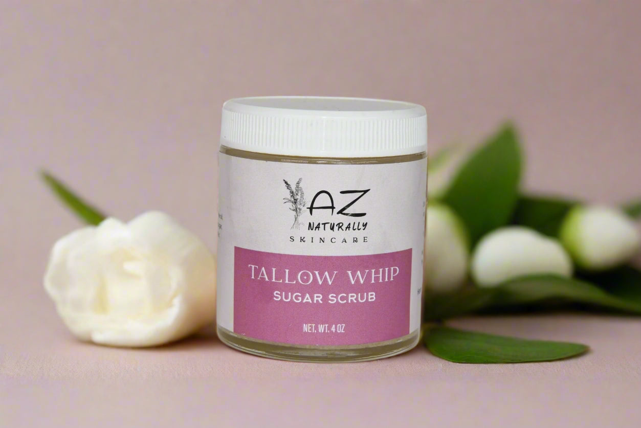 Jar of 'Tallow Whip Sugar Scrub' surrounded by leaves and white flowers 